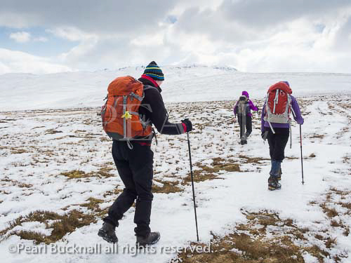 Three women Ramblers walking up Tal-y-Fan 
mountain in deep snow in mountains of Snowdonia 
National Park, Conwy, North Wales, UK, Britain