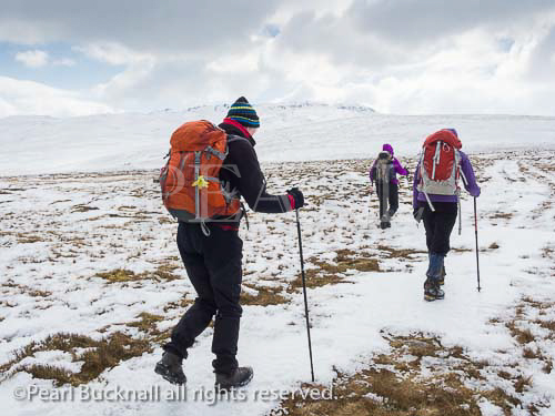 Three women Ramblers walking up Tal-y-Fan 
mountain in deep snow in mountains of Snowdonia 
National Park, Conwy, North Wales, UK, Britain