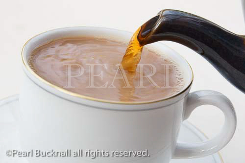 Pouring English tea into a white china teacup from a 
teapot spout. England, United Kingdom,Britain