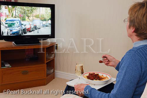 Mature woman sitting alone in front of the television 
eating a meal on a tray. UK, Britain. MR 11/14