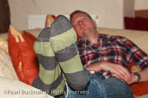 England UK Europe. A tired man wearing striped socks 
jeans and a check shirt sleeping on the living room 
sofa. England UK Britain Europe. 