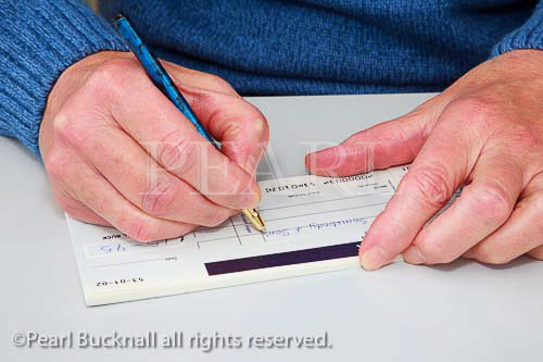 Close-up of a mature woman writing a cheque to pay 
a bill. England, UK, Britain
