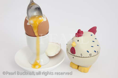 Spoon in an open soft boiled egg with runny yolk in an 
egg cup with a chicken egg timer

Keywords: food perfect timing novelty