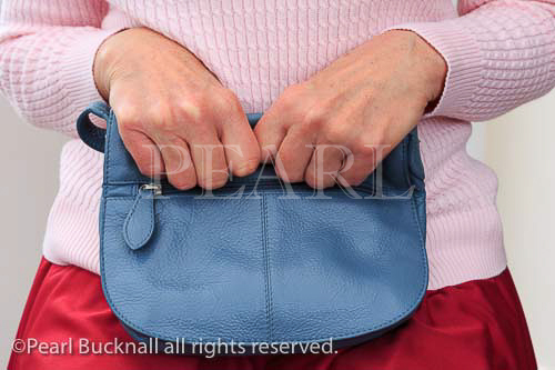 Senior woman sitting clutching a handbag with two 
hands close to her. UK, Britain. MR 13/27