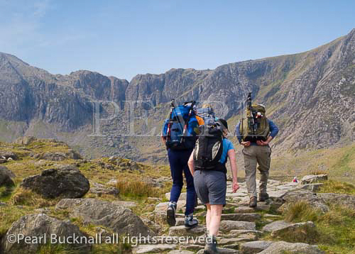 Group of people walking on footpath to Cwm Idwal 
with Devil's Kitchen beyond in Snowdonia National 
Park in summer. Ogwen North Wales UK Britain