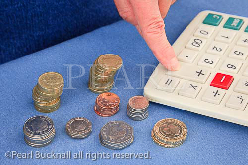 Person with a pile of British sterling coins using a 
calculator to count money. UK Britain MR 11/09