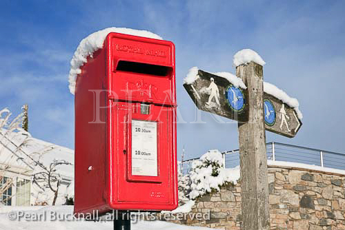 Red postbox and coastal path signpost in the snow. 
Red Wharf Bay, Isle of Anglesey, North Wales, UK, 
Europe

Keywords: British royal mail mailbox post letterbox 
Britain Welsh