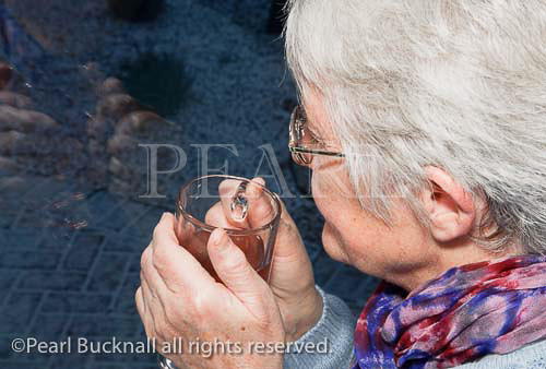 Senior woman holding a warm drink looking out of the
window on a cold dark night with snow outside in
winter. MR 10/47