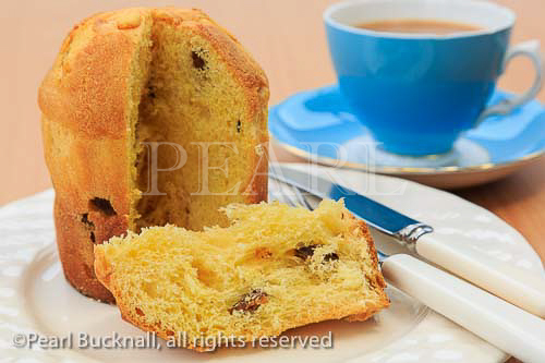 A slice of Panettone Italian Christmas fruit bread 
cake on a plate with a cup of tea on a table top. 