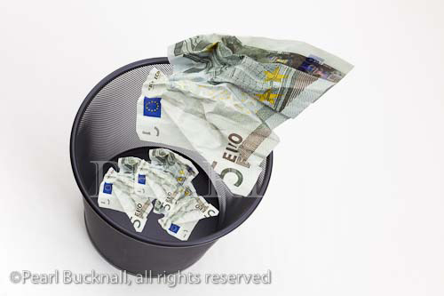 Five Euro notes being thrown into a black metal mesh 
waste paper bin

Keywords: digital compilation eurozone wasting 
money concept wastebasket throwing away