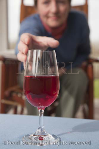 A mature woman sitting down reaching to pick up 
glass of red wine on a table. Britain UK Europe

Keywords: caucasian woman drinking alcohol