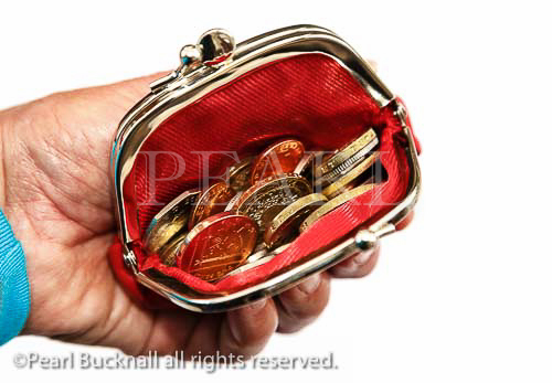 Senior pensioner holding a red purse open with 
money sterling coins in on a white background. 
England, UK, Britain, Europe