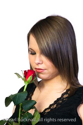 Portrait of a pretty young woman smelling a red rose 
on a white background