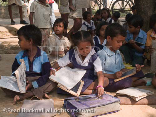 Junior school children sat on ground with books in 
shade of tree outside rural village school for outdoor 
lesson. Sania Madhya Pradesh India Asia