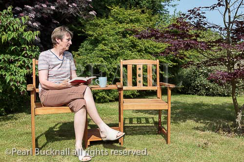 Senior woman looking sad sitting alone beside an 
empty seat in the garden in summer. UK, Britain