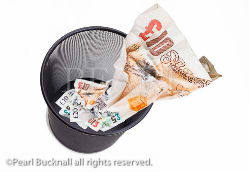 Composite image of a �10 note screwed up and 
being thrown away in a black waste paper bin on 
white from above to illustrate wasting money 
concept