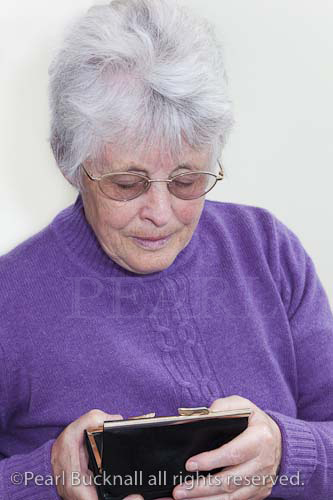 Senior woman looking into her purse with concerned 
expression. Britain UK Europe

money worries concept pensioner elderly person