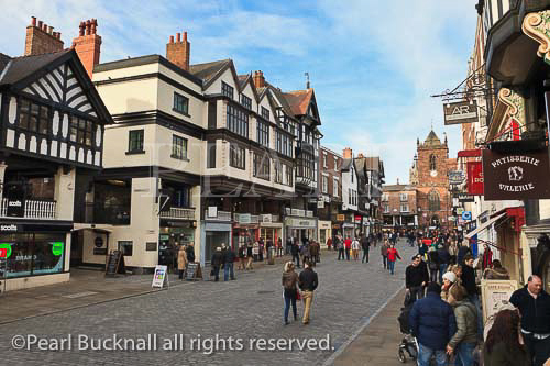Busy pedestrianised cobbled street scene with shops in 
historic buildings in the city centre. Bridge Street, 
Chester, Cheshire, England, UK, Britain, Europe. 