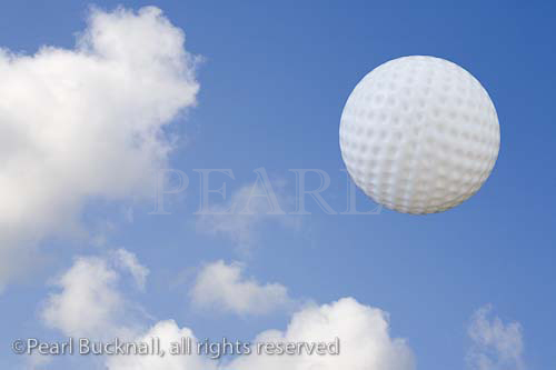 Golf ball flying across blue sky with white fluffy 
clouds.

Keywords: digital graphic sport equipment nobody