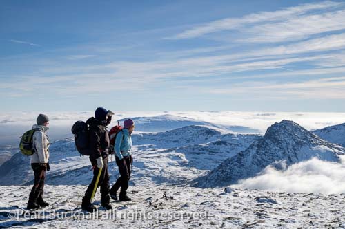 Three hikers on Pen Yr Ole Wen mountain summit with 
view to Mount Tryfan above low cloud in winter in 
mountains of Snowdonia National Park, North Wales, 
UK, Britain