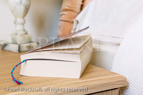 Paperback book on a bedside table at the side of a 
bed. England, UK, Britain, Europe