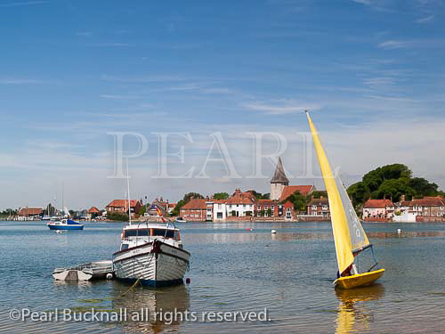 BOATS and YELLOW SAILING DINGHY in Bosham Creek 
in Chichester harbour at high tide with the village 
beyond in summer. Bosham, West Sussex, England, UK, 
Britain