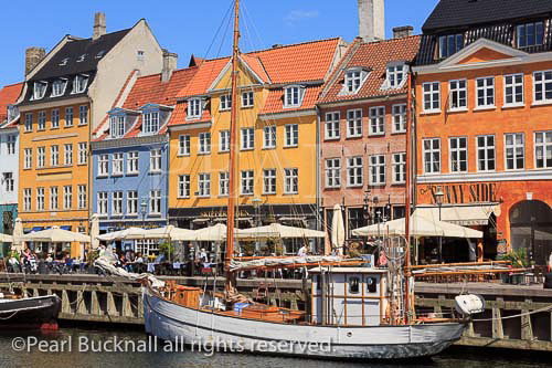 Old wooden boats moored on canal by pedestrianised 
waterfront street with outdoor cafes and colourful 
buildings in Nyhavn, Copenhagen, Zealand, Denmark, 
Europe