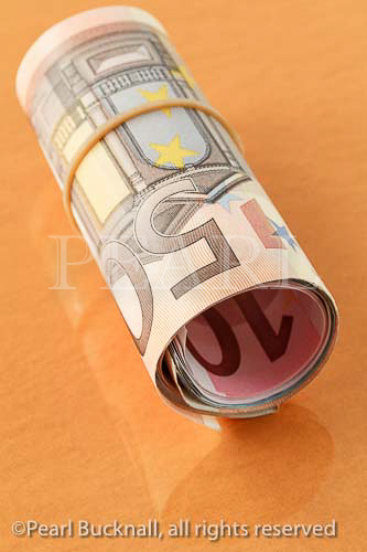 50 Euro note on a roll of Euros rolled up with an 
elastic band on a plain orange background