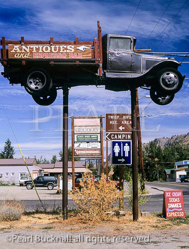 OLD TRUCK RAISED on POSTS and other 
advertisements by the crossroads on Highway 153 in a 
small town in Methow Valley. Twisp, Washington State, 
USA, North America