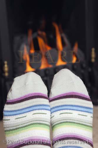Pair of feet wearing stripey wool socks warming in 
front of a coal gas fire in winter. UK Britain Europe


