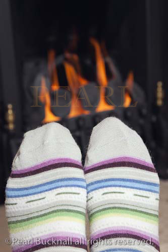Pair of feet wearing stripey wool socks warming in 
front of a coal gas fire in winter. UK Britain Europe


