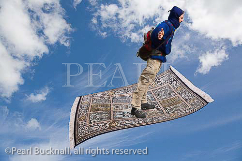 Man on a magic carpet flying up across blue sky with 
white clouds.