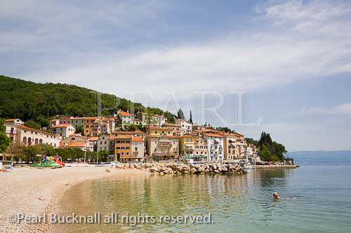 View along quiet beach to harbour and old town 
buildings on hillside in tourist resort on Kvarner coast 
of Istrian peninsula. Moscenicka Draga Istria Croatia 
Europe