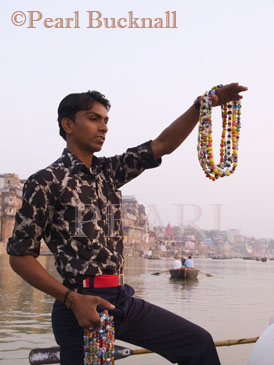 Indian man in boat holding strings of beads to sell to 
western tourists on sightseeing trip on River Ganges. 
Varanasi Uttar Pradesh India  Asia 
