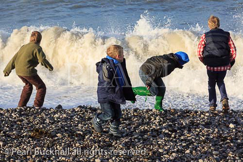 Children enjoy dodging waves at Penmon beach on 
Isle of Anglesey, North Wales, UK, Britain