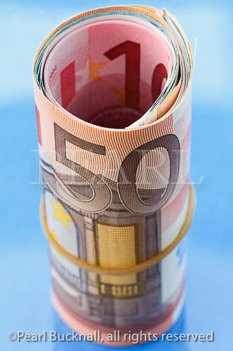 A 50 Euro note on a roll of Euros rolled up with an 
elastic band on a blue background