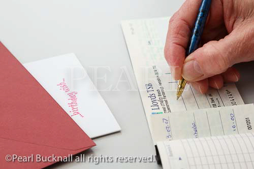 Female pensioner writing a Lloyds TSB cheque as a 
gift to put in a birthday card. England, UK, Great 
Britain