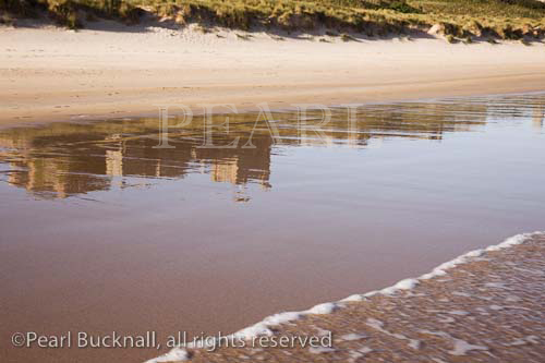 Bamburgh Castle reflected in wet sand on empty 
beach. Bamburgh, Northumberland, England, UK, 
Europe.

Keywords: British landmark English coast reflections 
sea