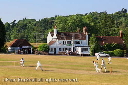 Local team playing a cricket match on the village green 
in front of the Barley Mow pub on a  summer's 
evening. Tilford, Surrey, England, UK, Britain