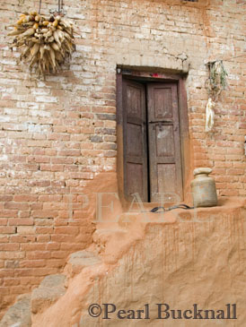 POT URN on TERRACOTTA STEPS to old wooden 
doorway in traditional style building with corn pods 
hanging to dry in rural village near Lalitpur. 
Bungamati, Kathmandu Valley, Nepal, Asia 
