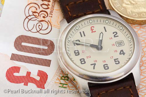 Man's wrist watch on a ten pound note and a coin for 
Time is Money concept. UK, Britain, Europe. 