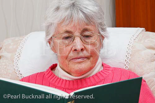 Elderly woman wearing spectacles sat reading a book. 
England, UK, Britain