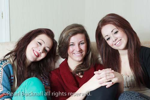 Three teenage friends aged 15 years sitting on a sofa 
together and smiling. UK Britain Europe. MR 