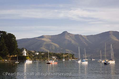 View to lighthouse across French Bay in picturesque 
historic seaside resort town on Banks Peninsula. 
Akaroa South Island New Zealand. 

