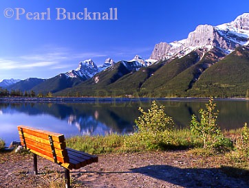 BENCH by THE RUNDLE RESERVOIR
with the forests and snowy peaks of the Rocky
Mountains reflected in the still water. Canmore,
Alberta, Canada, North America