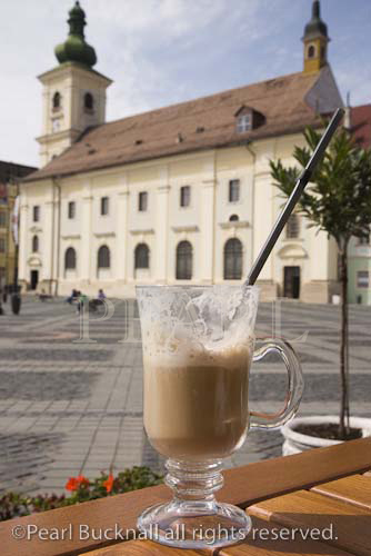 Latte Macchiato with straw in glass on table in street 
cafe in Piata Mare in historic city centre of 
Hermannstadt. Sibiu Transylvania Romania Europe
