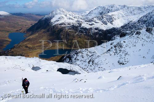 Hiker hiking in snow on Y Garn ridge with view to 
Ogwen Valley and Glyderau mountains in Snowdonia 
National Park. Ogwen, North Wales, UK, Britain