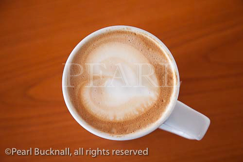 Mug of cafe Latte coffee with a heart shape in the 
froth on top of a wooden table from above