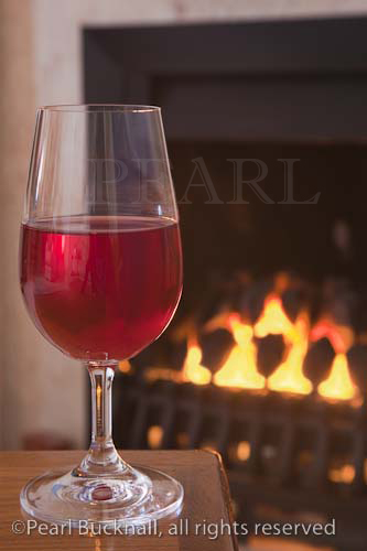 Glass of red wine on a table by an open coal fire

Keywords: still life alcohol homely fireplace warm 
room 