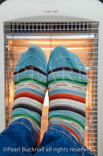 Person wearing colourful striped woolly socks 
warming feet in front of a low energy Halogen room 
heater. England UK Britain
